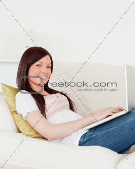 Cute red-haired woman relaxing with her laptop while lying on a 