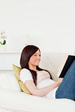 Charming red-haired woman reading a book while lying on a sofa