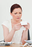Young attractive red-haired female studying a receipt while sitt