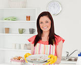 Attractive red-haired woman holding some dirty plates in the kit