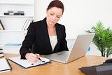 Young beautiful red-haired female in suit typing on her laptop a