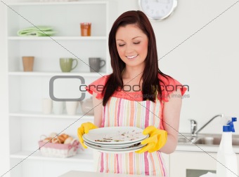 Good looking red-haired woman holding some dirty plates in the k