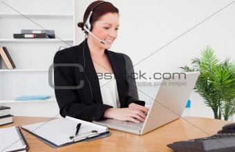 Young good looking red-haired female in suit typing on her lapto