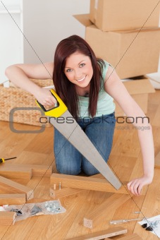 Good looking red-haired woman using a saw