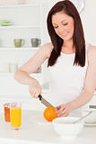 Young attractive red-haired woman cutting an orange in the kitch