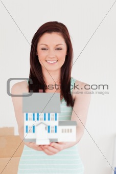 Good looking red-haired woman holding a miniature house while st