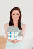 Pretty red-haired woman holding a miniature house while standing