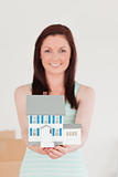 Cute red-haired woman holding a miniature house while standing o