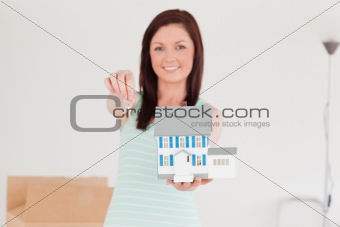 Good looking red-haired female holding a miniature house while s