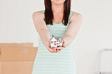 Cute red-haired female holding a miniature house while standing 