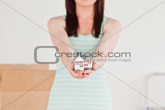 Cute red-haired female holding a miniature house while standing 