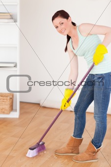 Good lookingl red-haired woman sweeping the floor at home