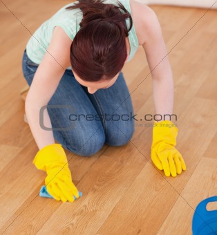 Attractive red-haired woman cleaning the floor while kneeling