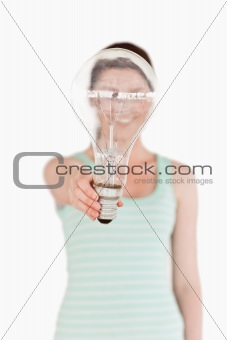 Pretty red-haired female holding a light bulb house while standi