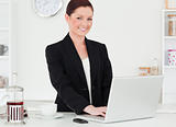 Pretty red-haired woman in suit relaxing with her laptop while p