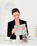 Good looking red-haired woman in suit reading the newspaper in t