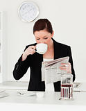 Good looking red-haired woman in suit reading the newspaper whil