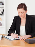 Beautiful red-haired woman in suit writing on a notepad