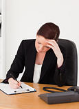 Depressed beautiful red-haired woman in suit writing on a notepa