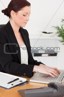 Young attractive red-haired woman in suit typing on her laptop
