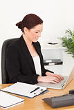 Young beautiful red-haired woman in suit typing on her laptop