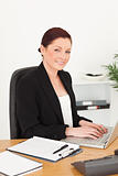 Young attractive red-haired woman in suit typing on her laptop a