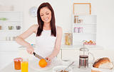 Young beautiful red-haired woman cutting an orange in the kitche
