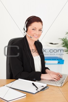 Young gorgeous red-haired woman in suit typing on her laptop and