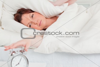 Charming red-haired woman waking up thanks to an alarm clock