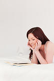 Pretty red-haired woman reading a book while lying on her bed