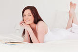 Attractive red-haired woman reading a book while lying on her be