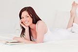 Good looking red-haired woman reading a book while lying on her 