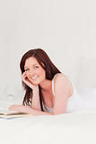 Charming red-haired woman reading a book while lying on her bed