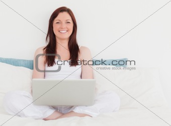 Pretty red-haired female relaxing with her laptop while sitting 