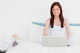 Attractive red-haired woman relaxing with her laptop while sitti