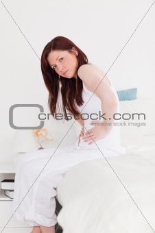 Attractive red-haired female posing while sitting on her bed