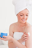 Cute young woman wearing a towel using skin cream