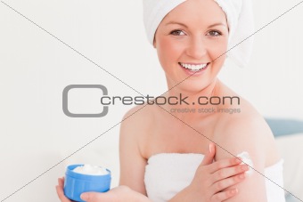 Beautiful young female wearing a towel using skin cream