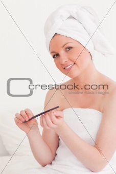 Beautiful young woman wearing a towel using a nail file