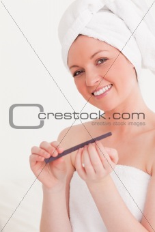 Attractive young woman wrapped in a towel using a nail file 