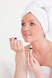 Good looking young woman wearing a towel using a lip gloss