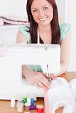 Pretty red-haired woman using a sewing machine in the living roo