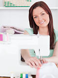 Attractive red-haired woman using a sewing machine in the living