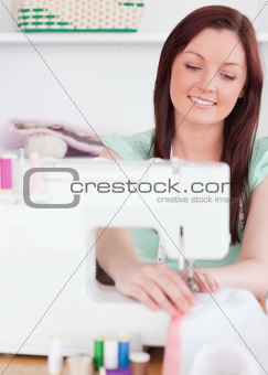 Good looking red-haired woman using a sewing machine in the livi