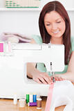 Gorgeous red-haired woman using a sewing machine in the living r