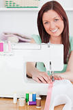 Charming red-haired woman using a sewing machine in the living r