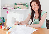 Attractive red-haired female using a sewing machine in the livin
