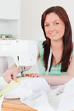 Good looking red-haired female using a sewing machine in the liv