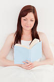 Beautiful red-haired female reading a book while sitting on her 