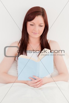 Beautiful red-haired female reading a book while sitting on her 